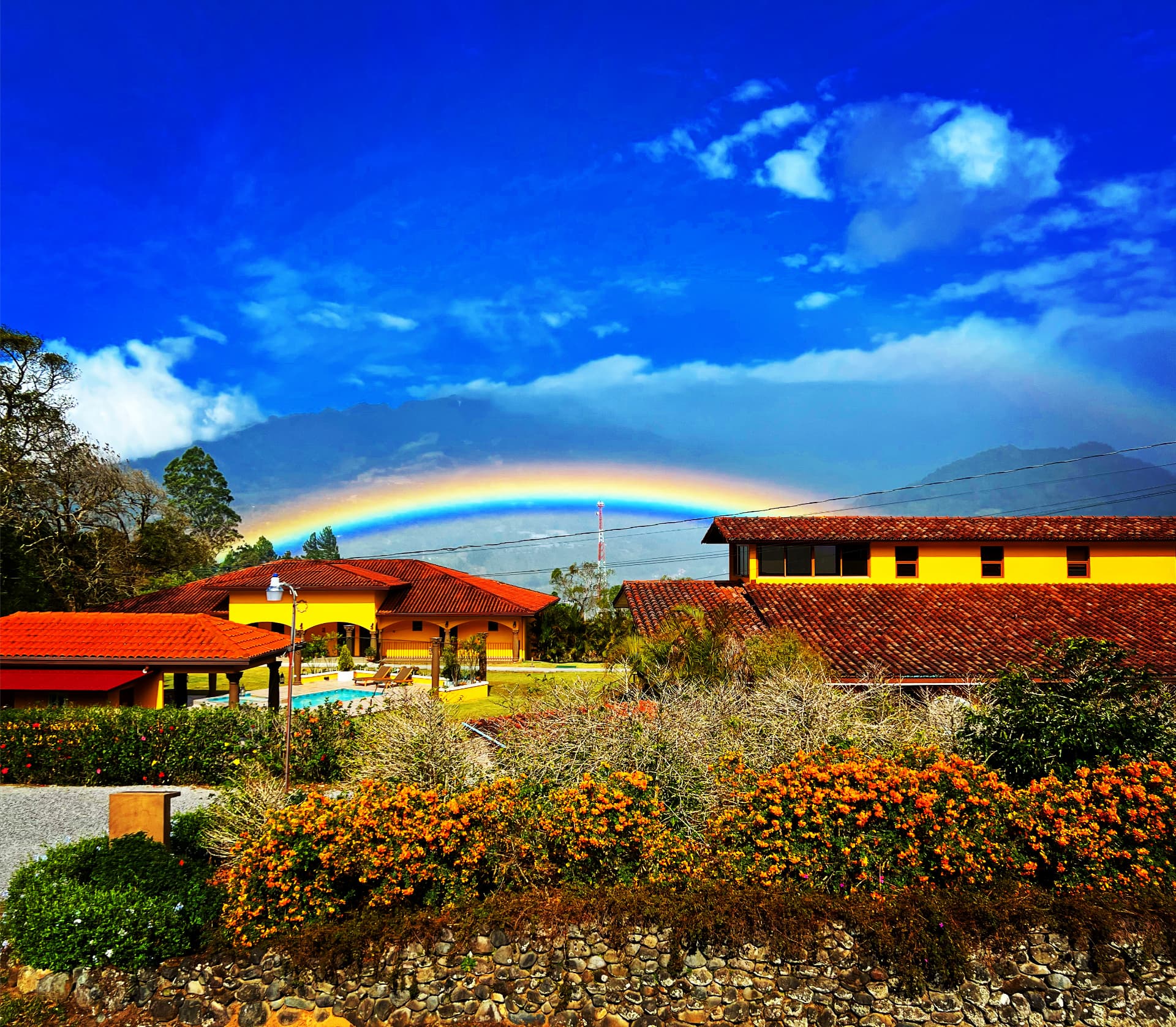 A vibrant double rainbow arcing over yellow houses and lush green hills in Panama