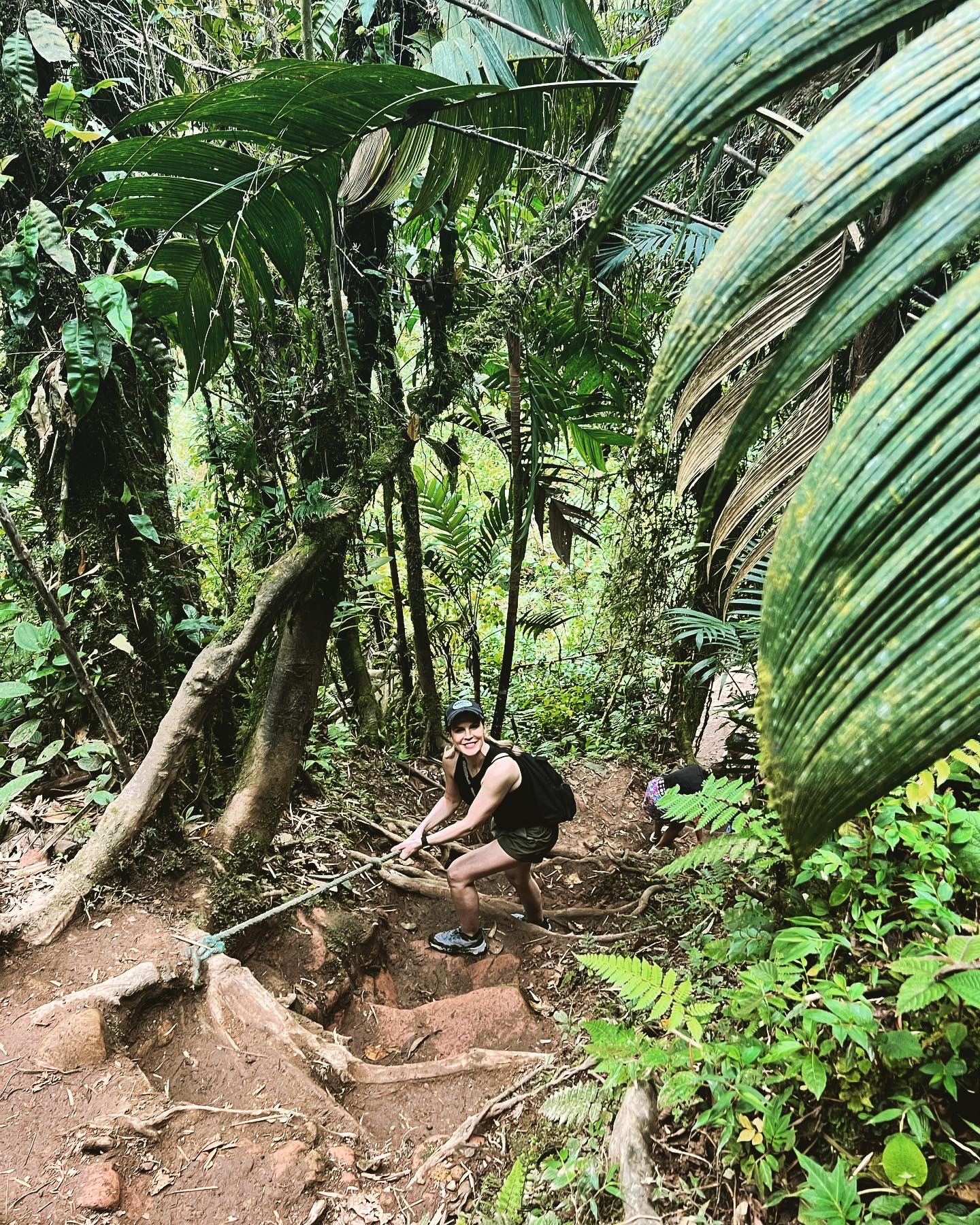 Tara Housh climbing a steep, root-covered jungle trail with the help of a rope in Boquete, Panama